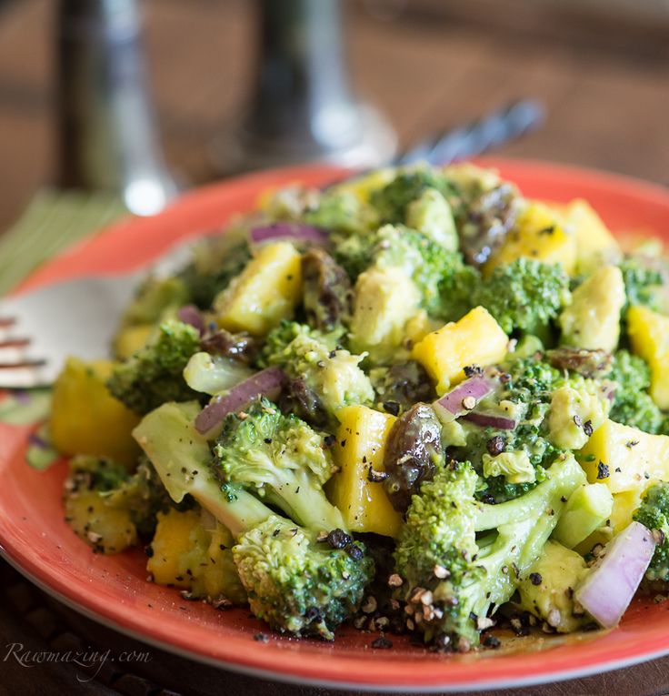 broccoli and pineapple salad on an orange plate with silverware in the background