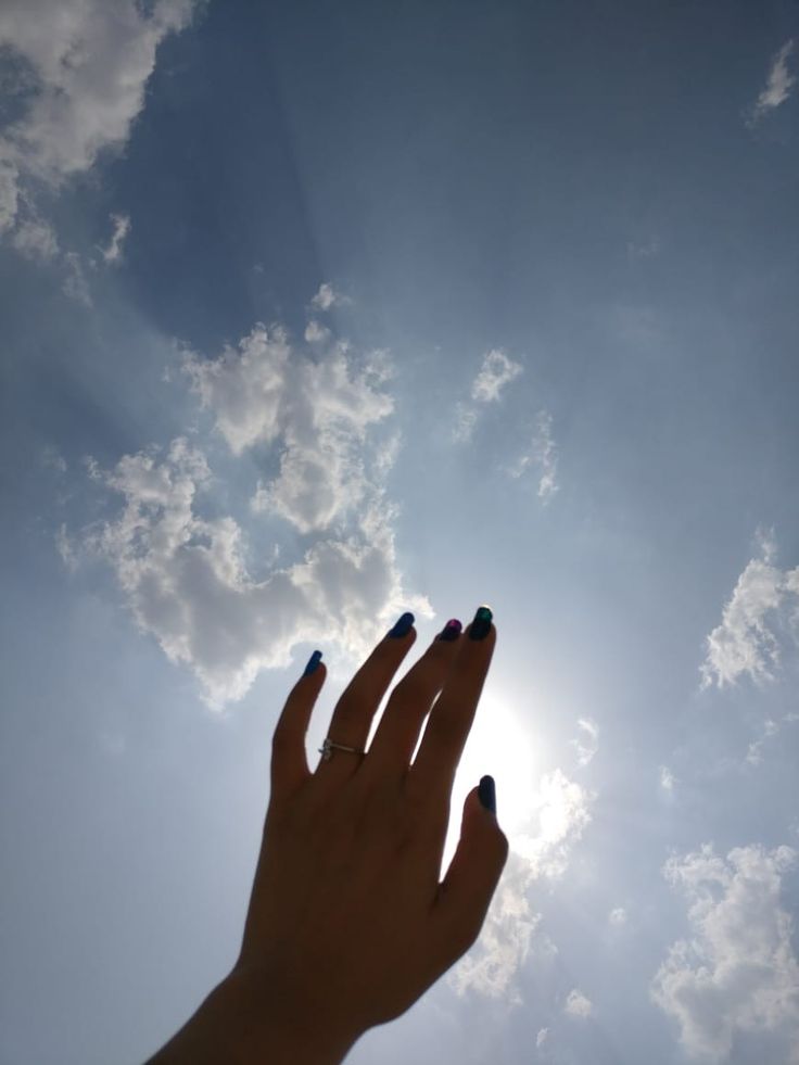 a person's hand reaching up into the sky with clouds in the back ground