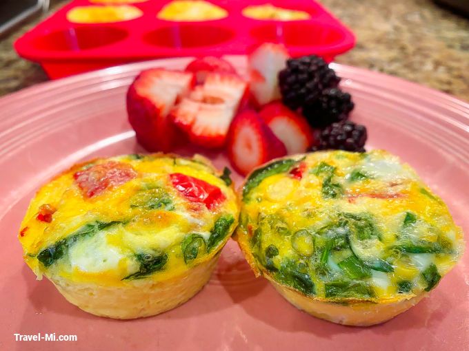 two muffins on a pink plate with strawberries and other fruit in the background