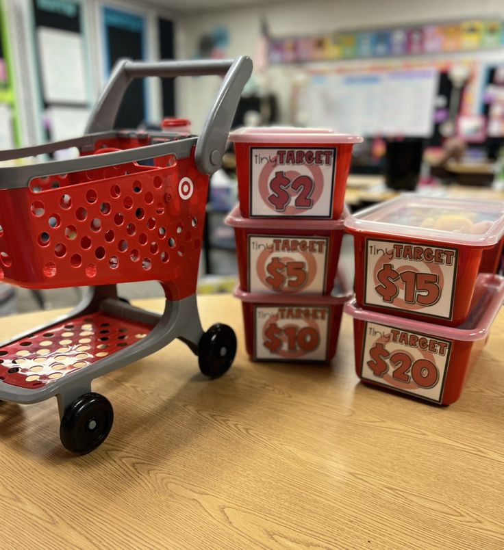 a red shopping cart sitting on top of a wooden table next to small plastic containers