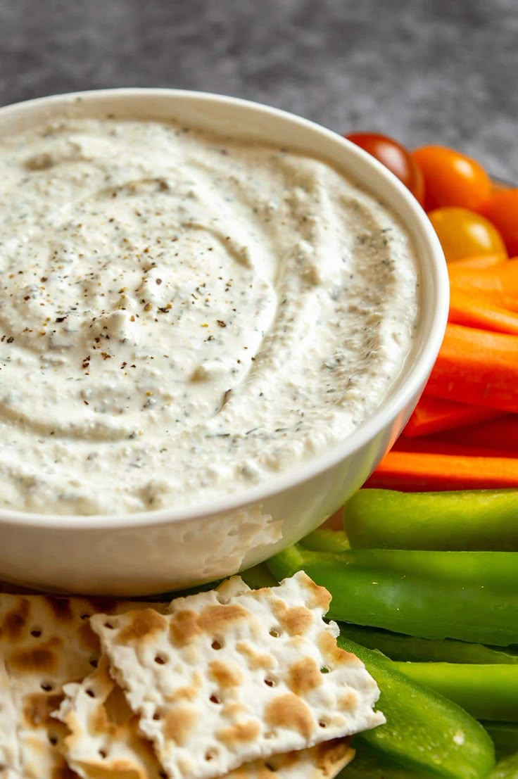 a white bowl filled with cheese dip surrounded by crackers and vegetables