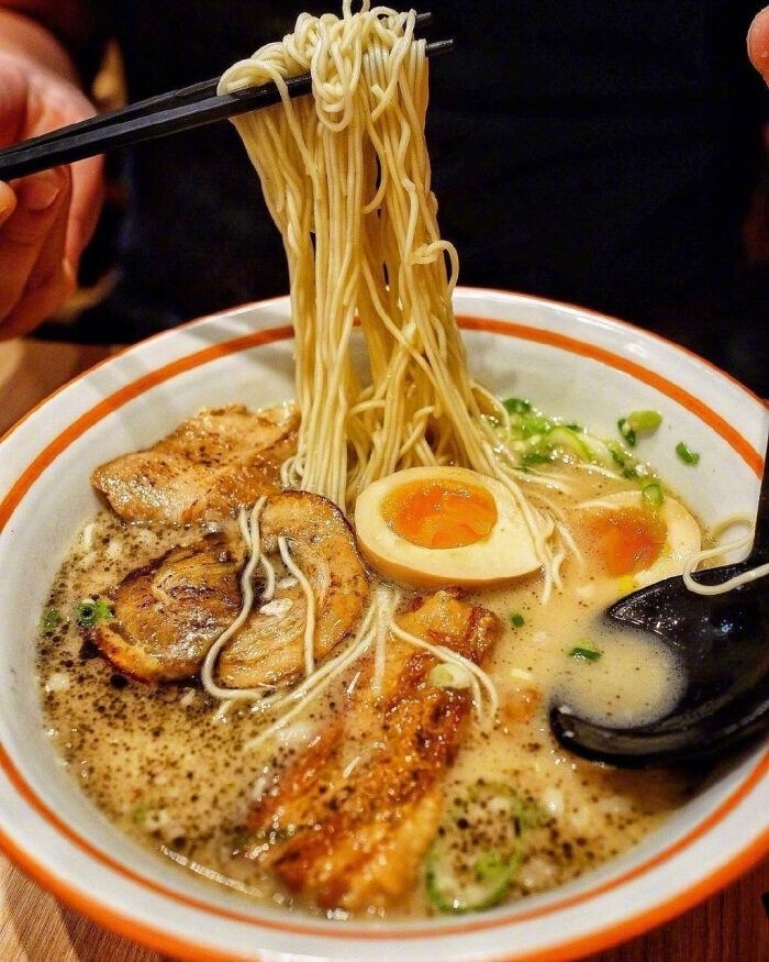 someone is holding chopsticks over a bowl of ramen with noodles and meat