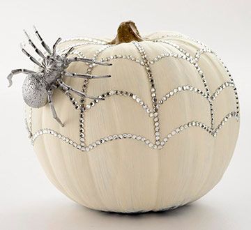 a white pumpkin decorated with silver beads and a spider sitting on it's side