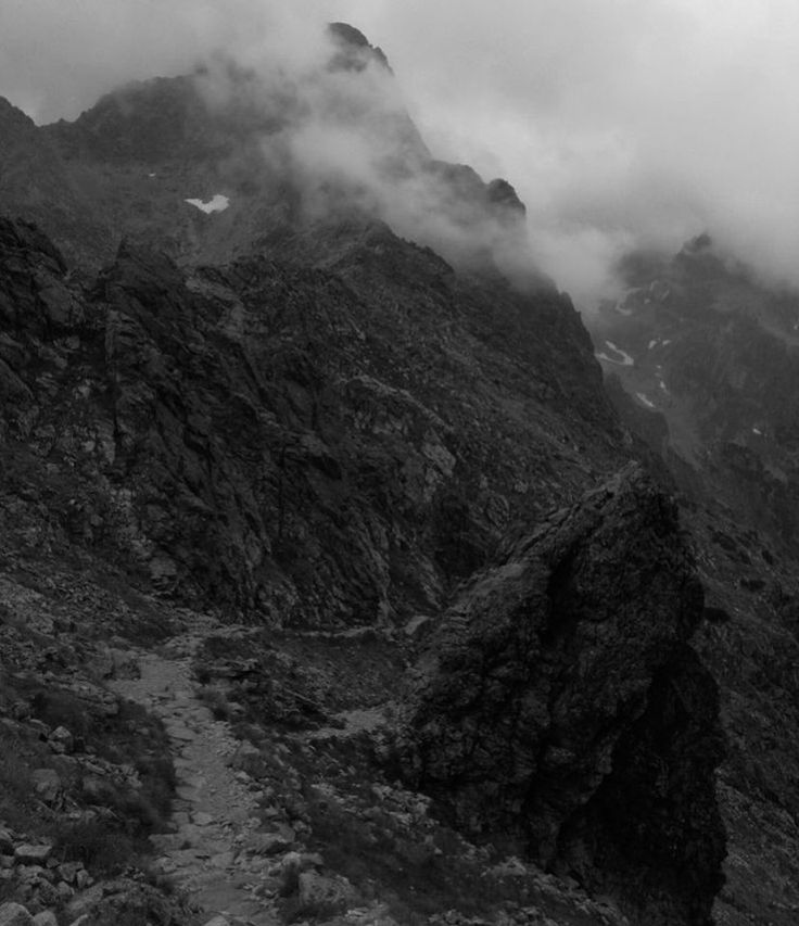 black and white photo of mountains with clouds in the sky on a foggy day