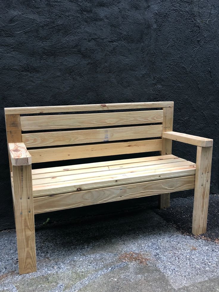 a wooden bench sitting in front of a black wall with gravel on the ground next to it