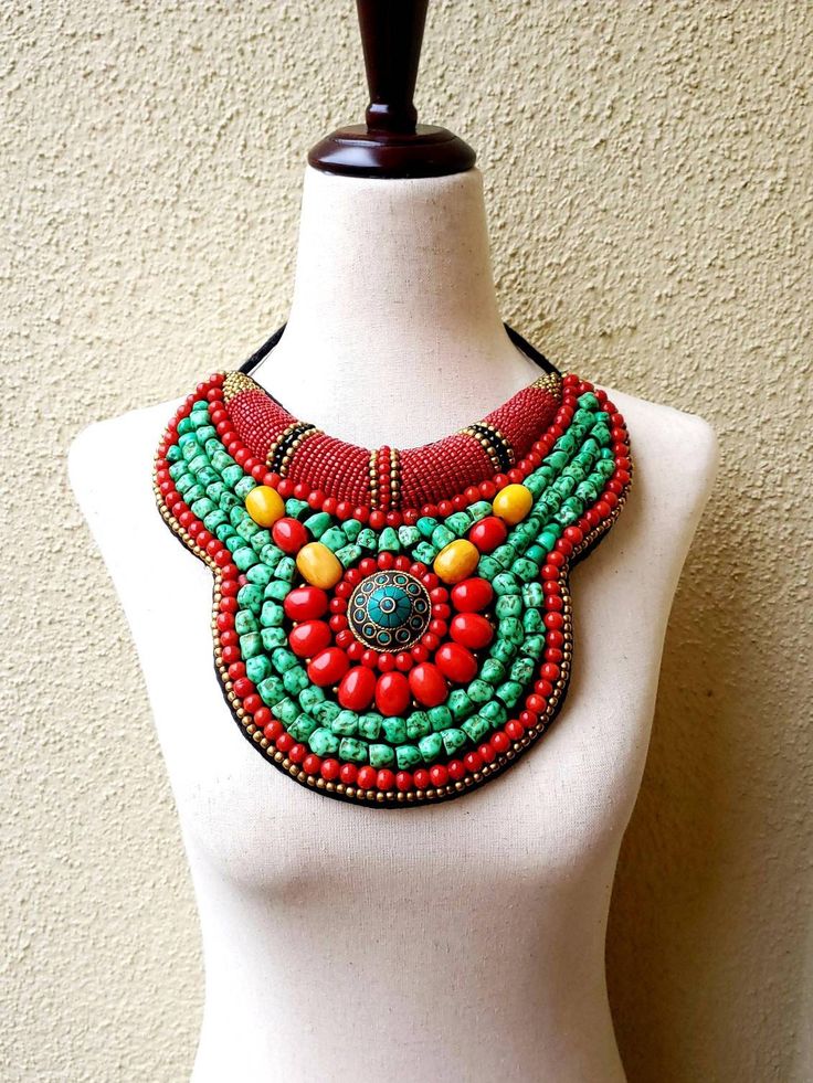 "Striking Tibetan turquoise and coral bib collar necklace in faux teal green turquoise, coral and amber beads, with a stunning central brass medallion. Perfect with a flowing caftan or an itsy black bikini. Perfect anywhere you are barefoot! Wear your hair up, with a bright ribbon or turban, or wear it down! You don't need much else! Eye-catching geometric pattern with a mix of smooth and textured beads. This is a handmade reproduction of a Tibetan tribal neck piece or Skeypuk, which is worn as Bohemian Turquoise Bib Necklace With Colorful Beads, Red Bohemian Bib Necklace For Festivals, Handmade Turquoise Bohemian Bib Necklace, Bohemian Red Bib Necklace With Round Beads, Green Bohemian Beaded Necklaces, Red Beaded Bohemian Bib Necklaces, Bohemian Bib Necklace With Colorful Beads, Green Turquoise Necklace With Colorful Beads For Festivals, Bohemian Beaded Necklaces With Round Beads