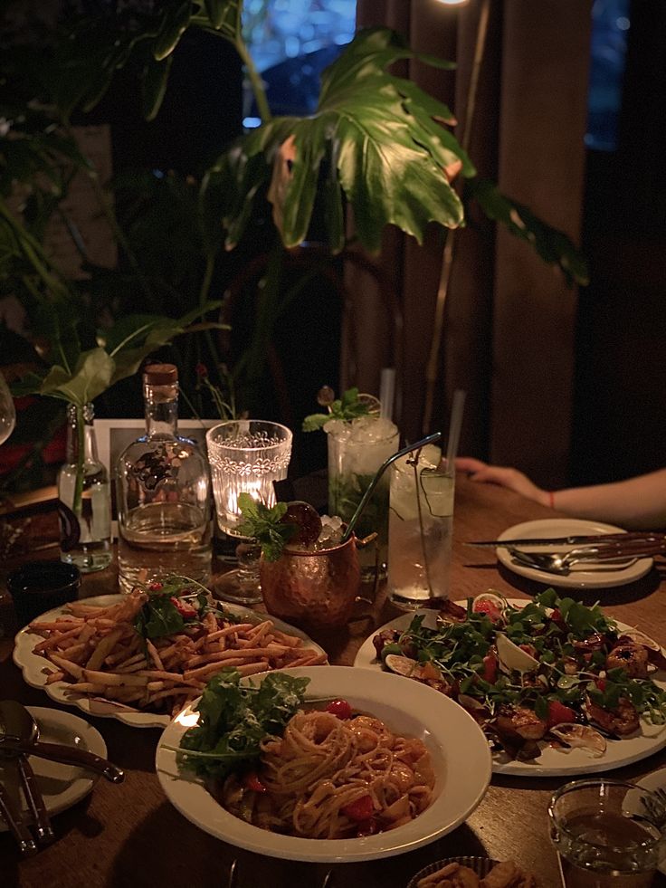 the table is set with many plates of food and drinks, including salads and pasta