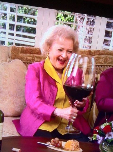 an older woman holding a glass of wine in her hand and laughing at the camera