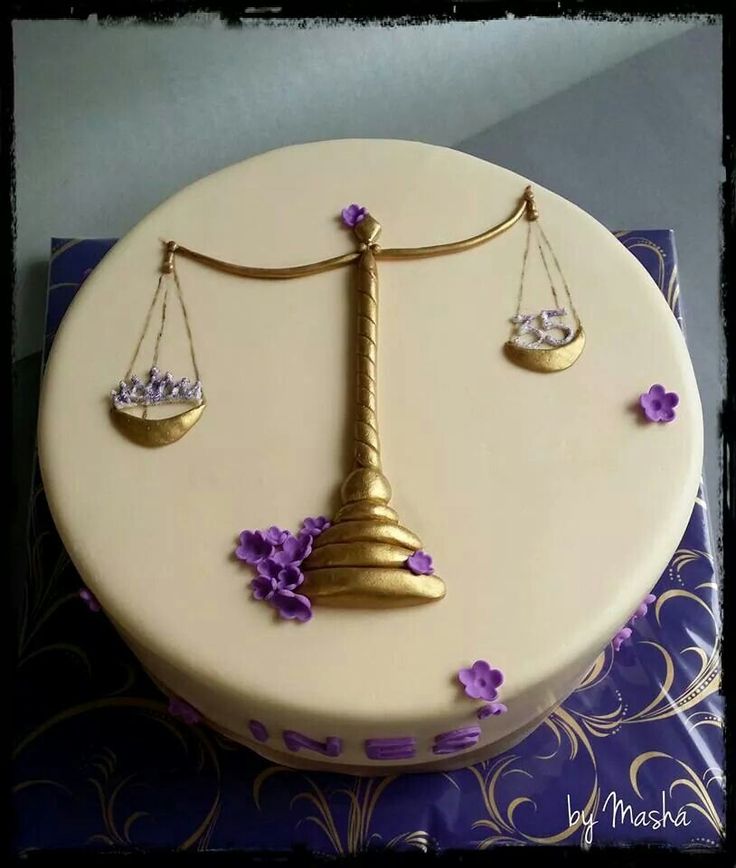 a white cake with purple flowers on it and a gold balance scale on the top