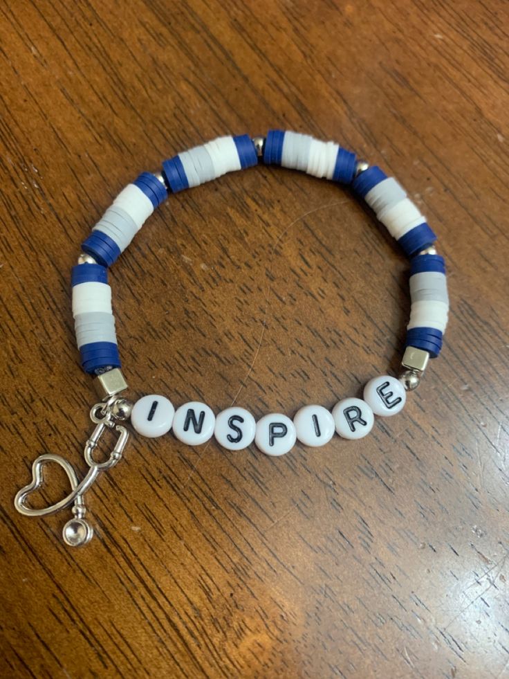 a bracelet with the word inspire on it sitting on top of a wooden table next to a pair of scissors