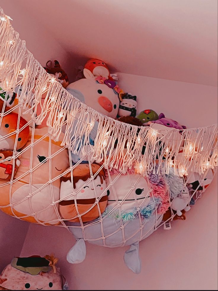 a hammock filled with stuffed animals on top of a pink wall covered in string lights