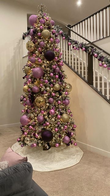 a purple and gold christmas tree in a living room with stairs leading up to the second floor