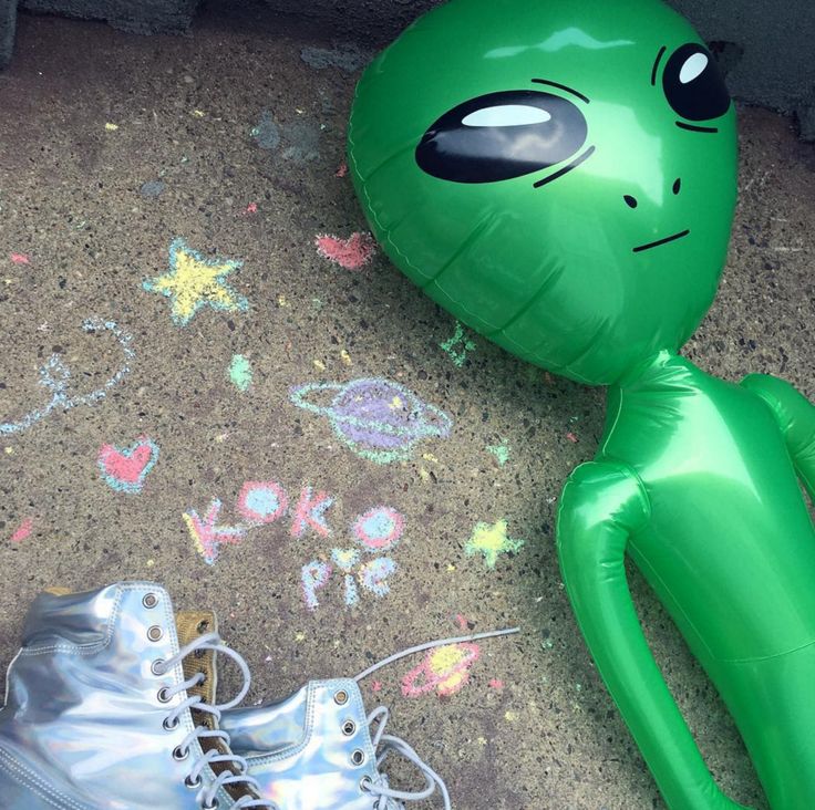 an inflatable alien doll laying on the ground next to a pair of shoes