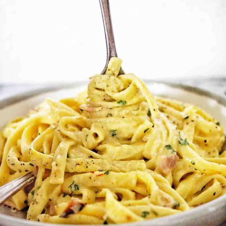 a fork full of pasta with sauce and parmesan cheese on the top, in a white bowl