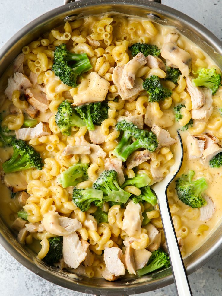 a pot filled with pasta and broccoli on top of a table next to a spoon