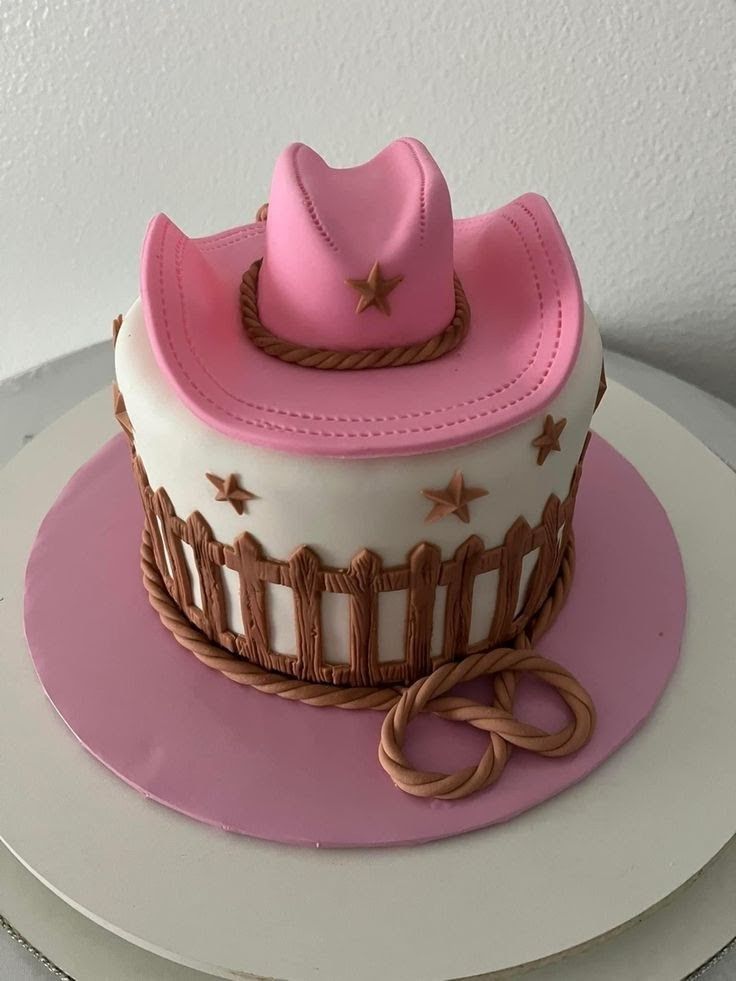 a pink and white cake with a cowboy hat on top, sitting on a plate