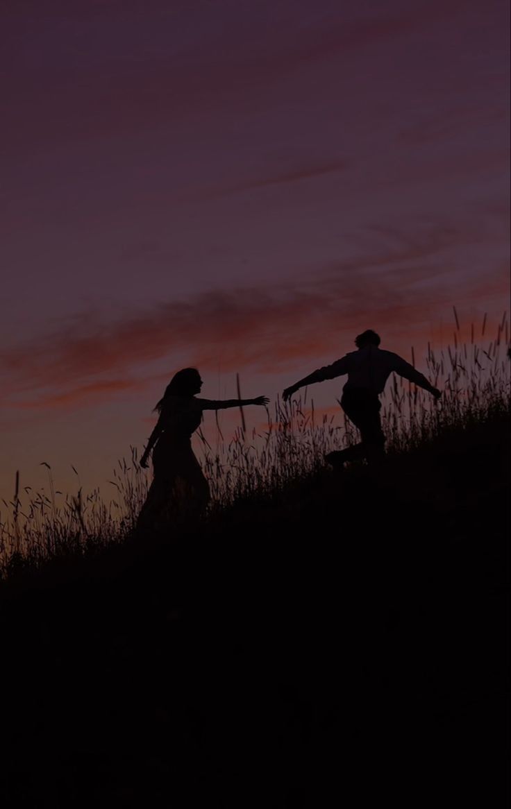 two people are walking up a hill at sunset with their arms outstretched in the air