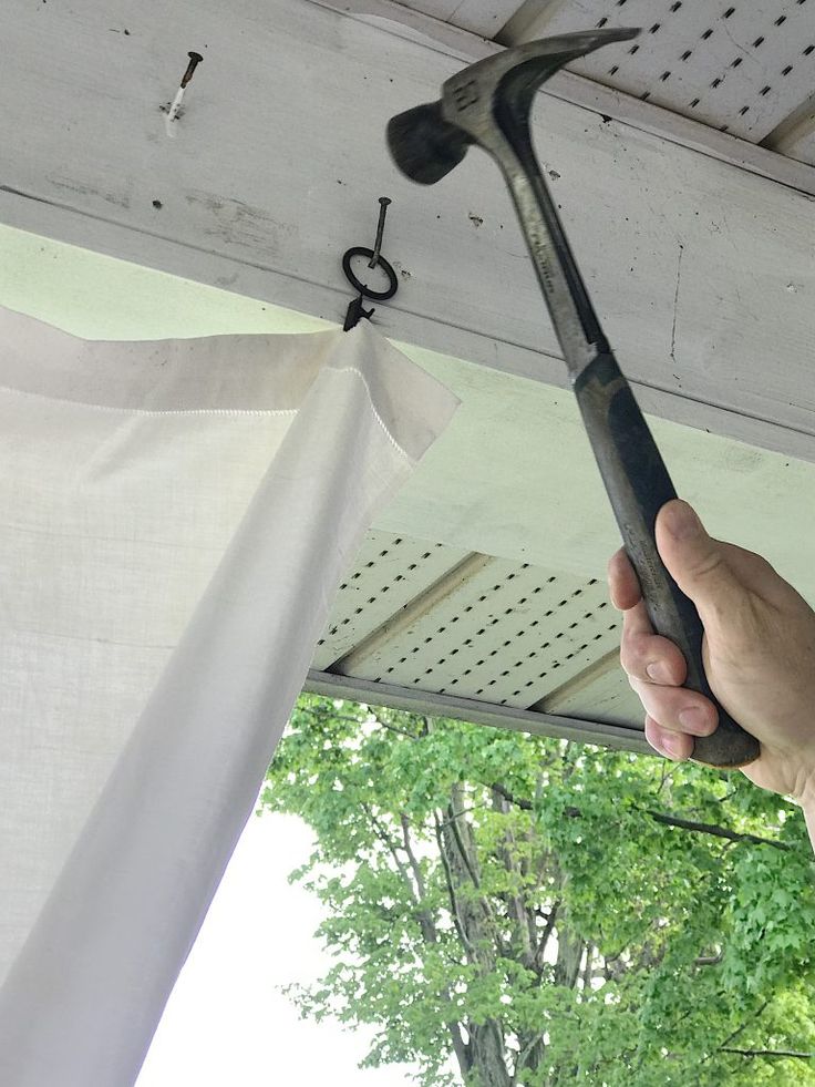 a hand holding an old hammer in front of a white drapes with trees in the background