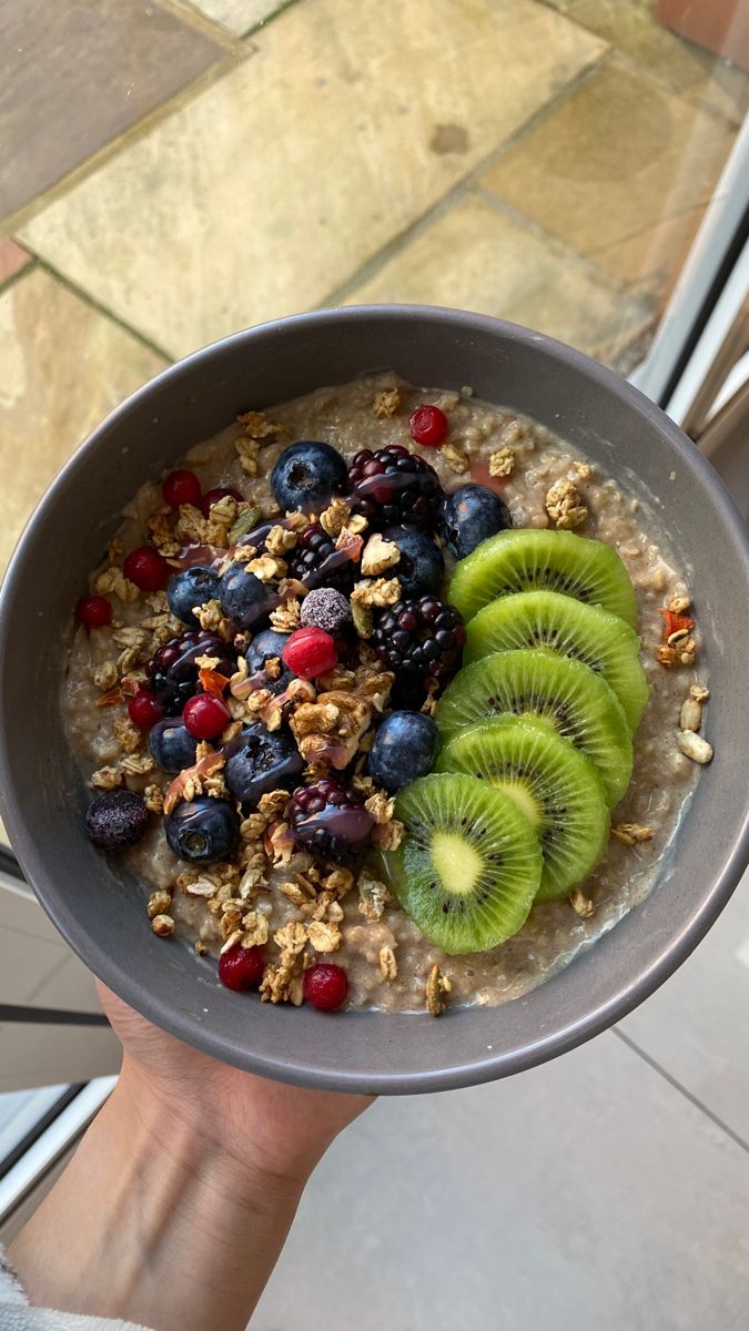 a person holding a bowl of oatmeal with kiwis and berries