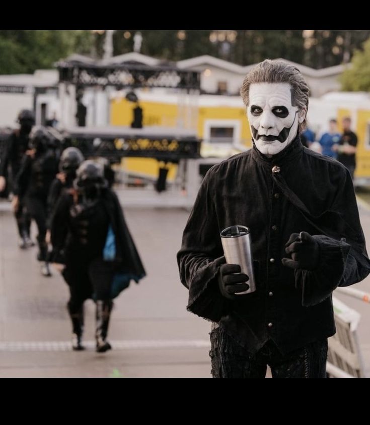 a group of people dressed in costumes walking down the street with one person wearing a mask and holding a cup