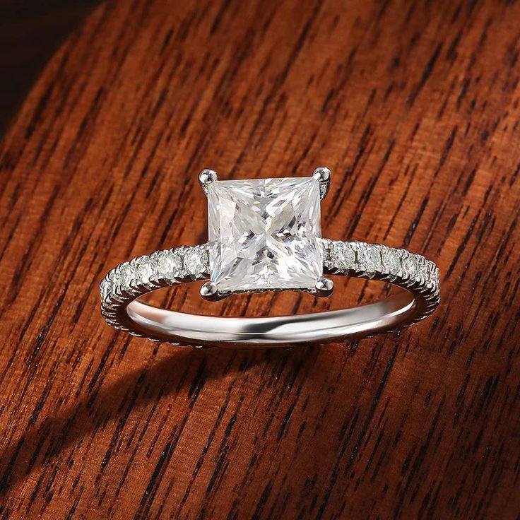 a princess cut diamond engagement ring on top of a wooden table with diamonds around the band