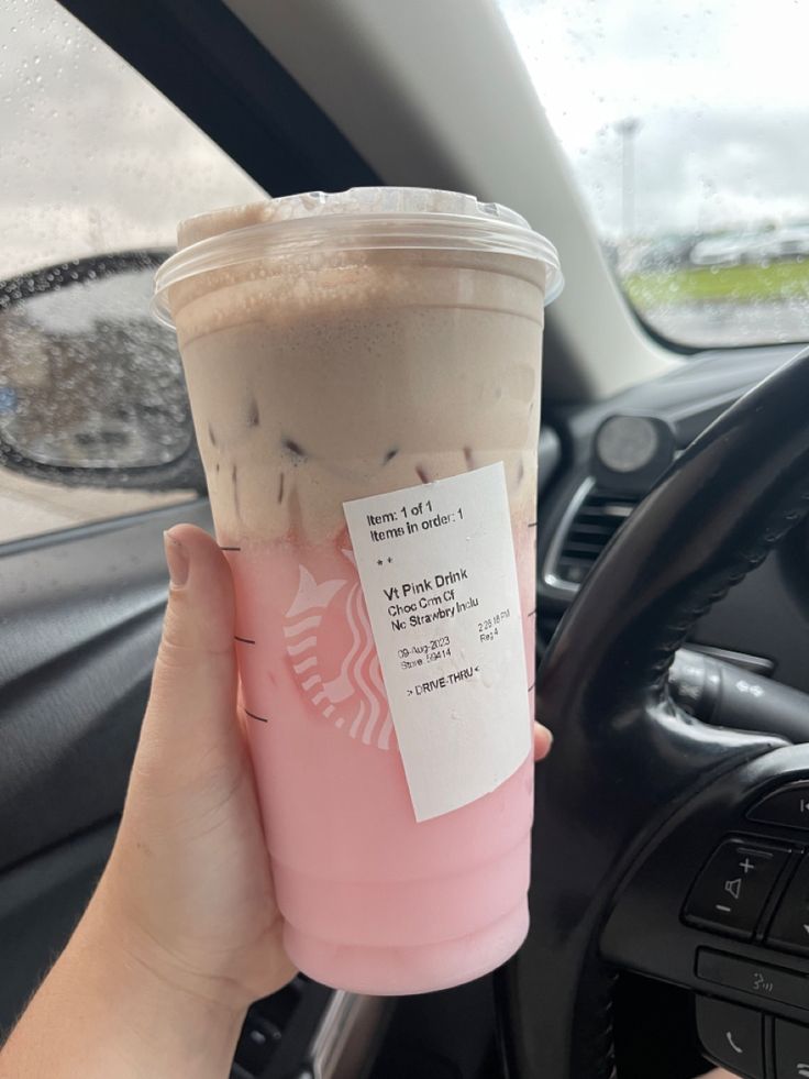 a person holding up a cup of coffee in their hand and steering wheel behind the car