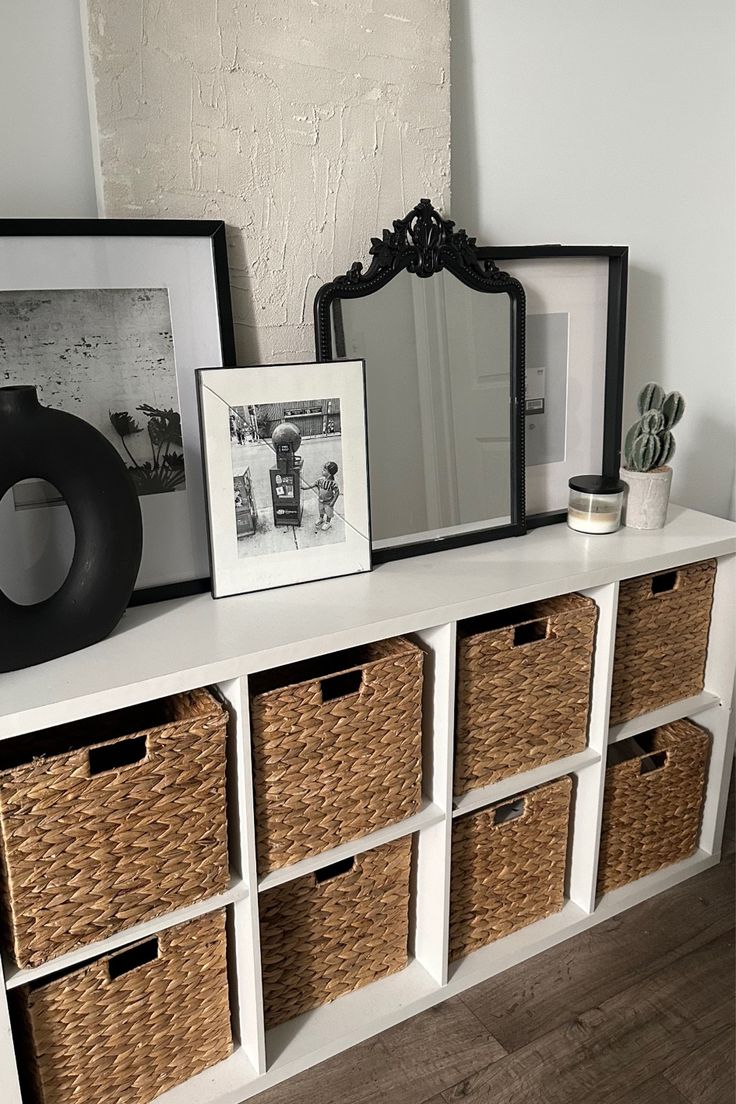 a white shelf with baskets and pictures on it next to a mirror, framed photograph, and other items