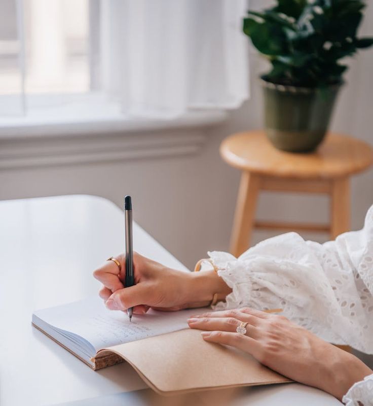 a woman sitting at a table writing on a notepad with a pen in her hand