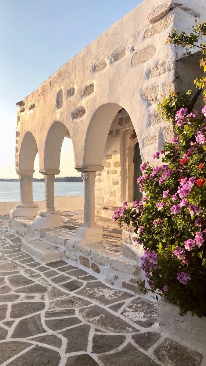 an old stone building with arches and flowers growing on the wall next to it in front of water