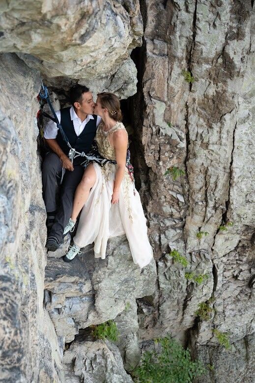 a man and woman are sitting on the side of a rock face each other as they kiss