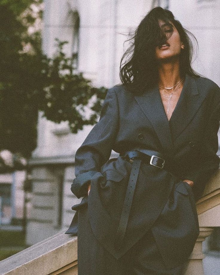 a woman leaning against a wall with her hands on her hips wearing a black suit