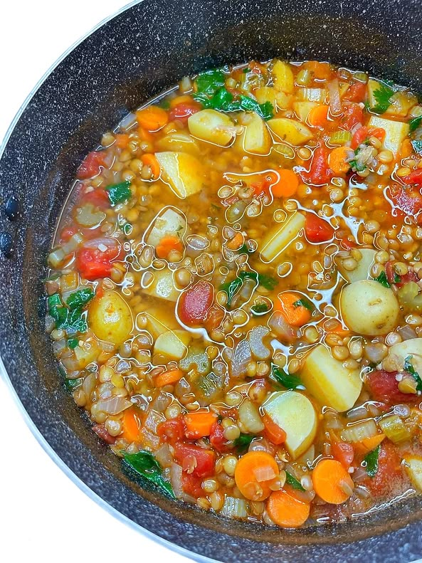 a bowl full of soup with carrots, potatoes and spinach