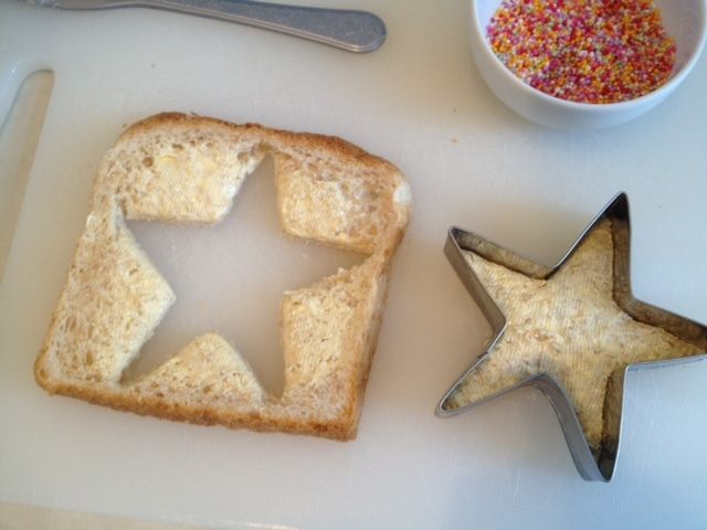 two star shaped cookies next to a bowl of sprinkles and a spoon