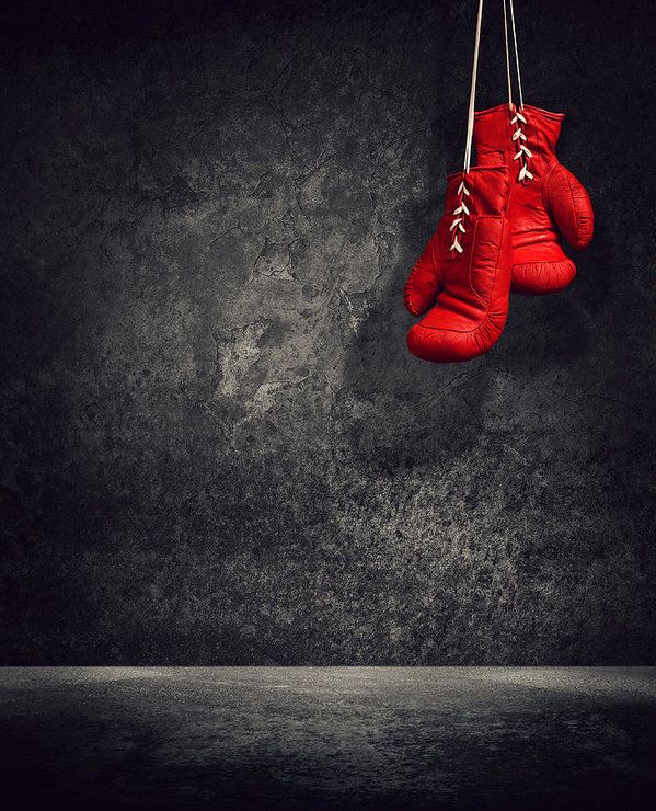 pair of red boxing gloves hanging from rope against dark grungy wall with water below