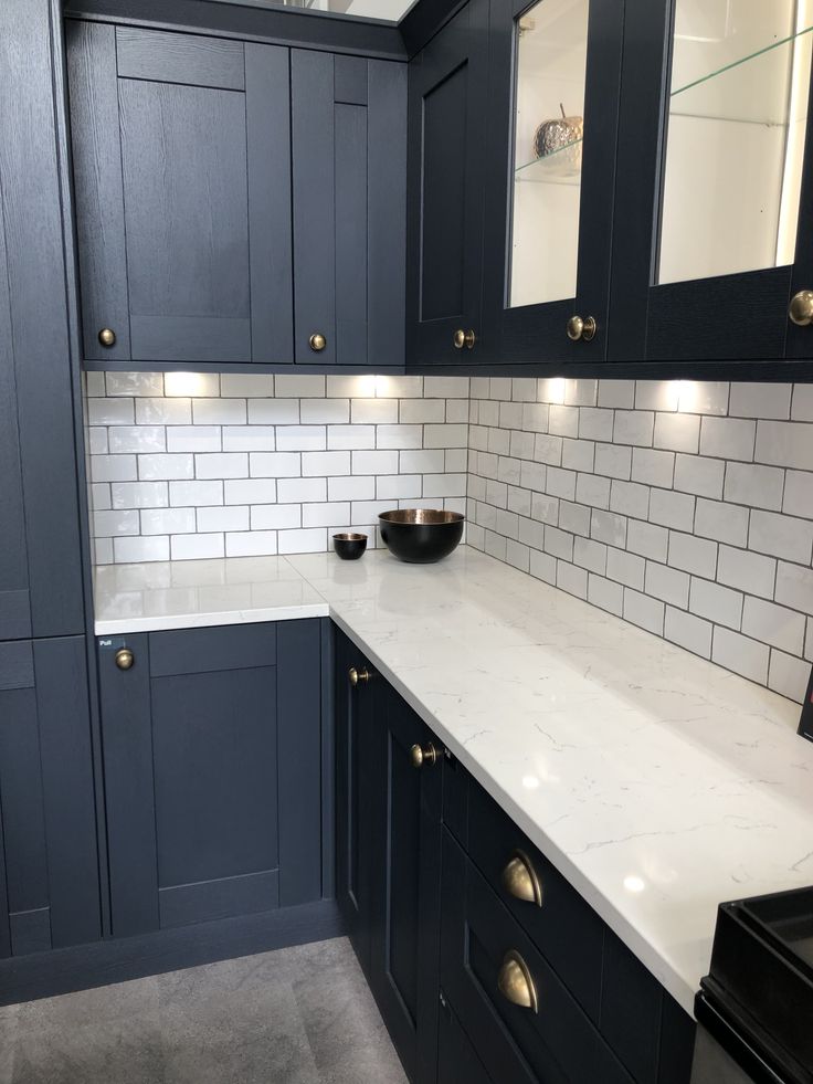 a kitchen with dark blue cabinets and white counter tops, gold pulls on the cupboards