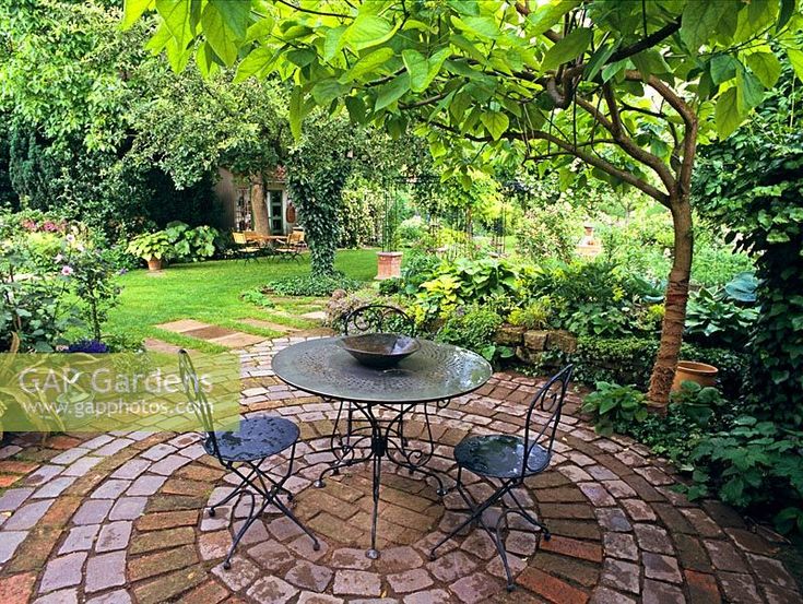 an outdoor table and chairs in the middle of a brick patio surrounded by greenery