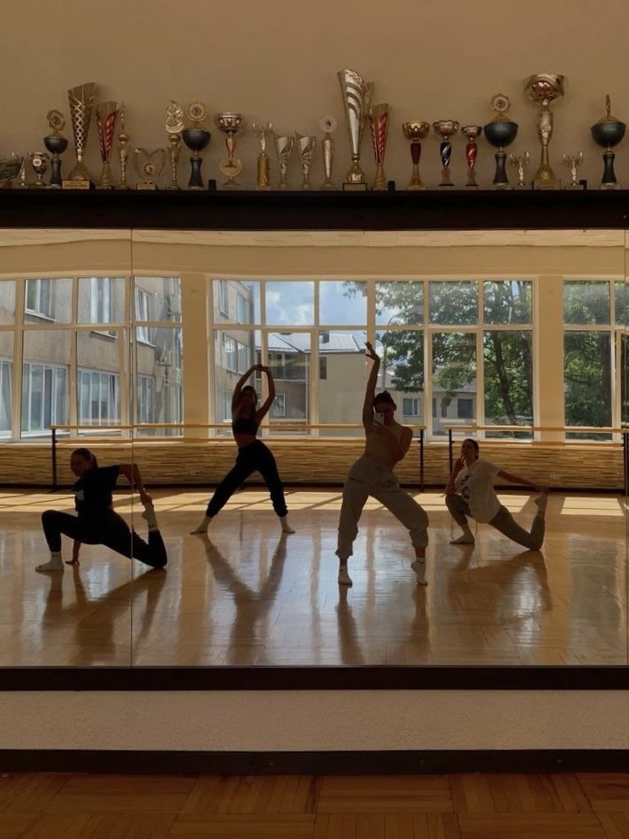 five people doing yoga poses in front of large windows with trophies on the wall behind them