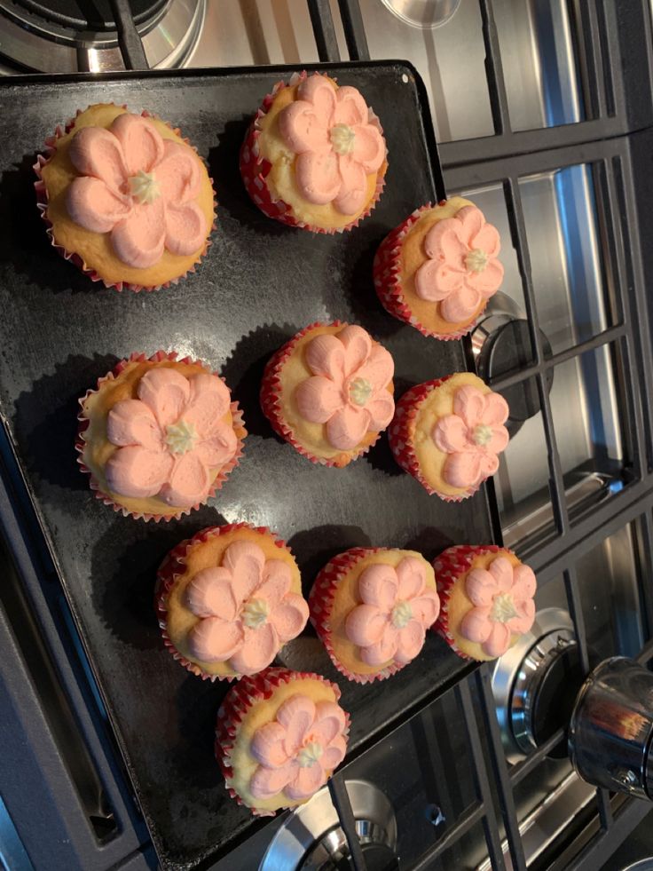 twelve cupcakes sitting on top of a baking sheet in an oven with pink frosting