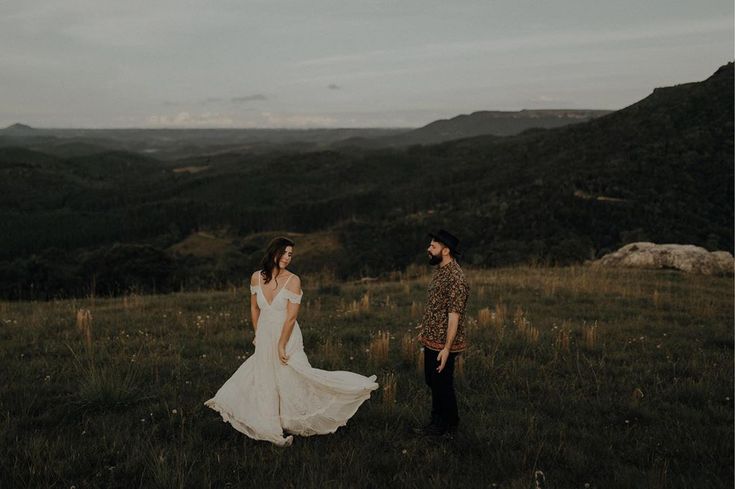 a man and woman standing on top of a lush green hillside