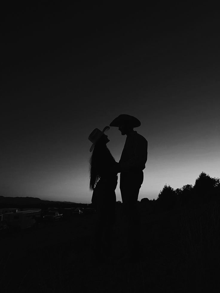 a man and woman standing under an umbrella in the dark at sunset or dawn, silhouetted against a darkened sky