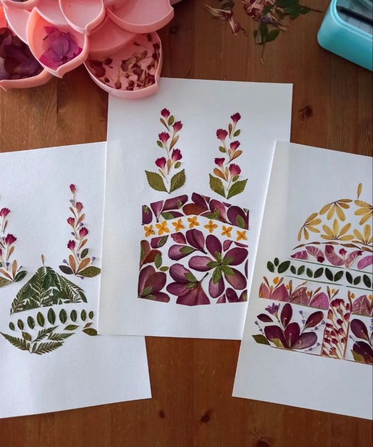 three cards with designs on them sitting on a table next to some flowers and bowls