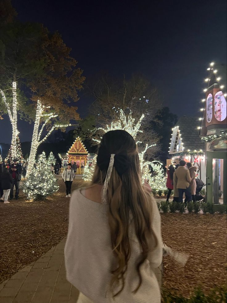 a girl is standing in front of christmas lights at the park with her back to the camera