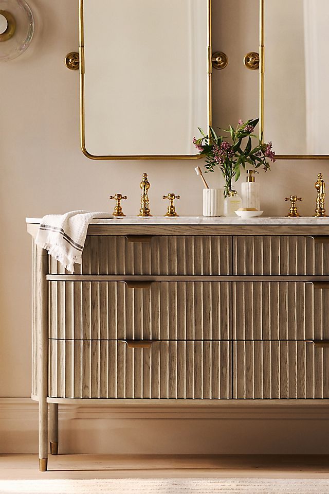 a bathroom vanity with two mirrors above it and flowers in vases on the counter