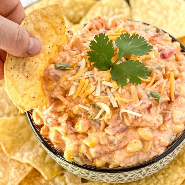 a hand dipping a tortilla chip into a bowl filled with salsa and chips