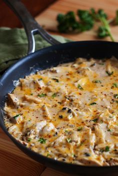 a skillet filled with chicken and cheese on top of a wooden table next to broccoli