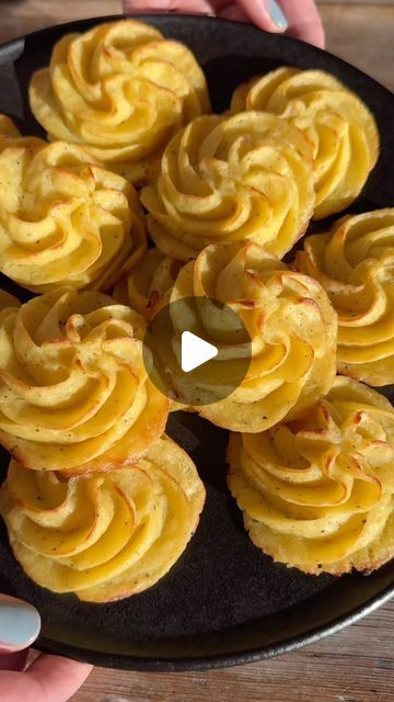 a black plate topped with yellow cupcakes on top of a wooden table next to a person