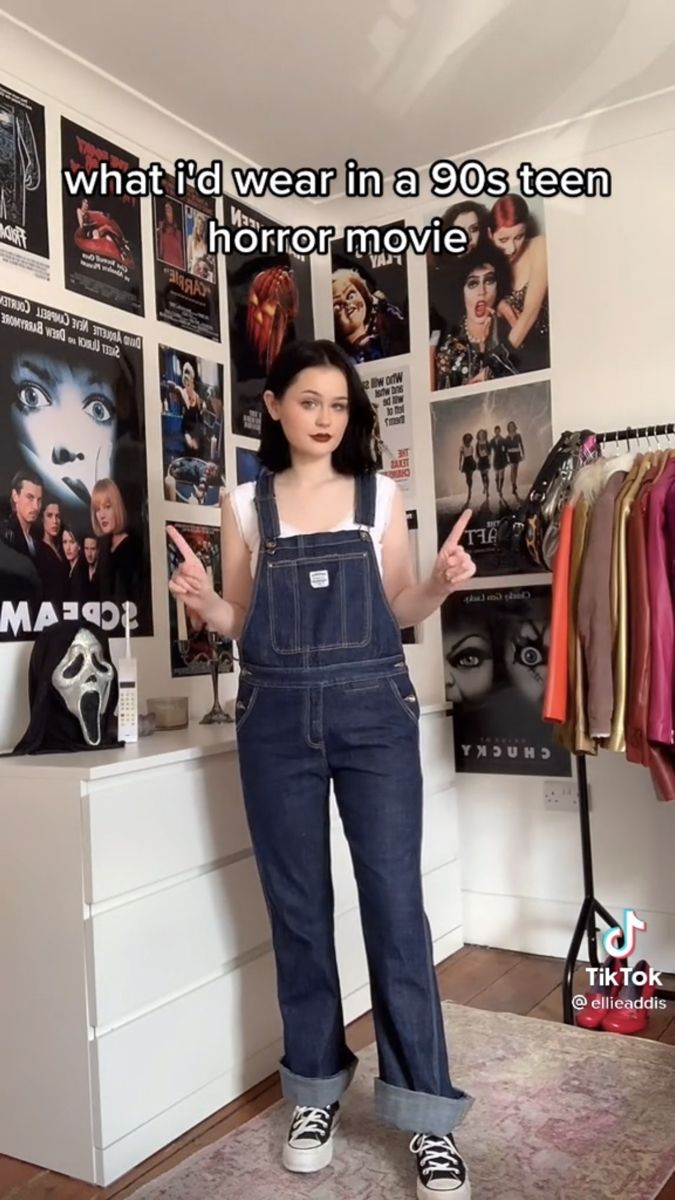 a woman standing in front of a wall with posters on it and the caption what i'd wear in a 90's teen horror movie