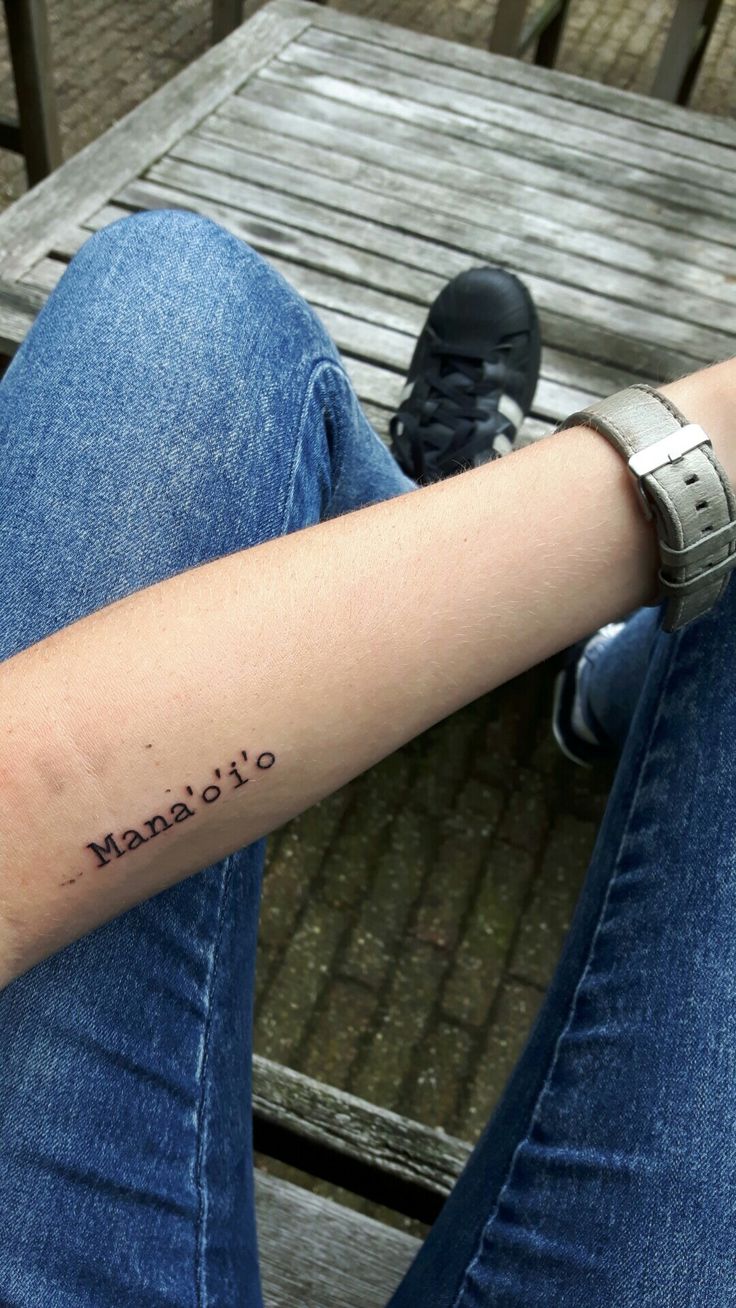 a woman's arm with the word utopia tattooed on her left forearm, sitting in front of a wooden bench