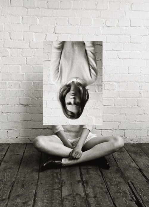 a woman is sitting on the floor with her hands behind her head, in front of a brick wall