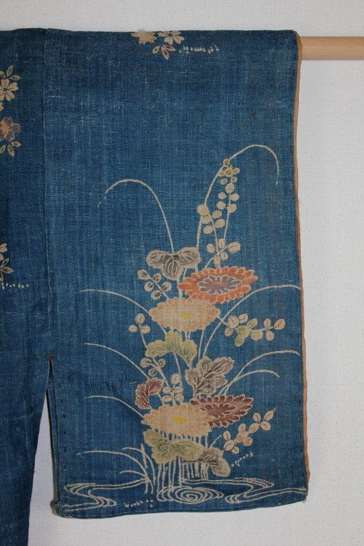 an old piece of cloth with flowers on it hanging from a wooden hanger next to a white wall